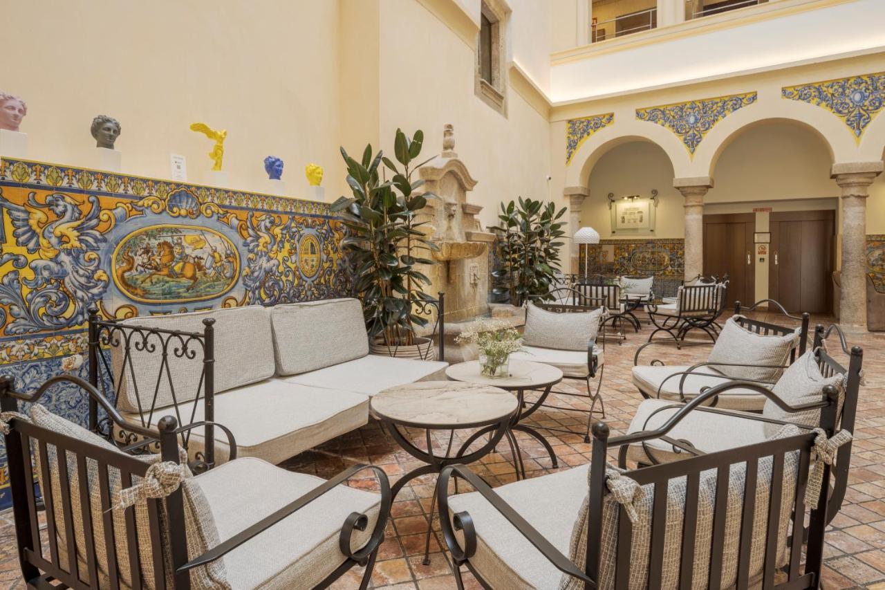 Hotel Ilunion Merida Palace Exterior photo The photo shows a beautifully designed indoor lounge area. It features several comfortable seating arrangements with cushions, arranged around a central table. The decor includes colorful tiled murals on the walls, and there are decorative plants add