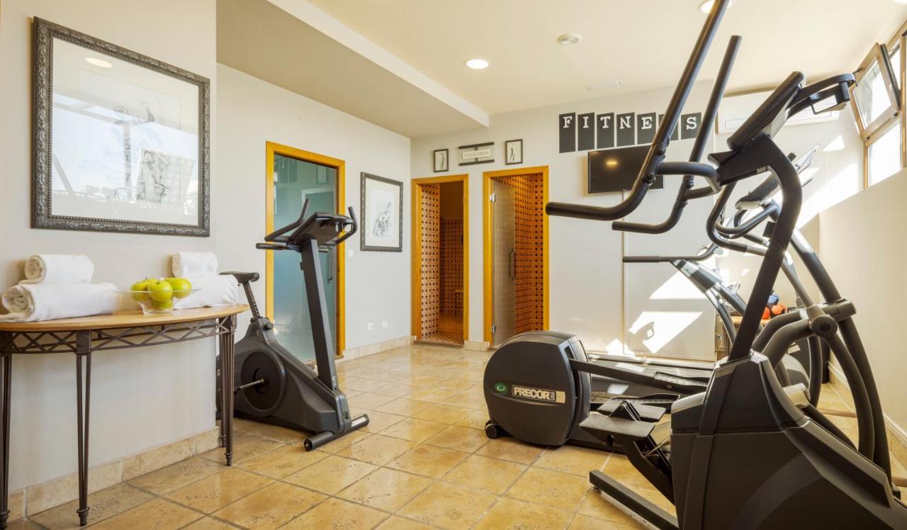 Hotel Ilunion Merida Palace Exterior photo The photo shows a fitness room equipped with various exercise machines. There are elliptical and stationary bikes positioned in the space. The flooring appears to be tiled, and the room has large windows allowing natural light to enter. On the wall, 